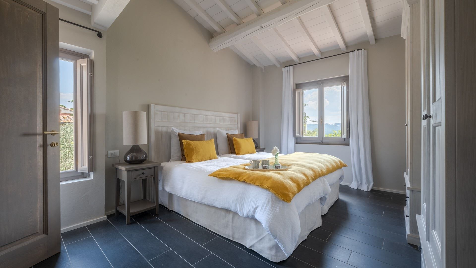 A bedroom with a large bed, a nightstand, a window with curtains, and a view of the outdoors.