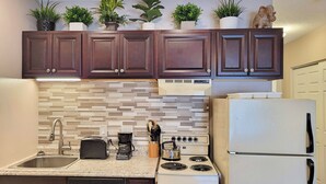 A modern kitchen with dark wooden cabinets, a tiled backsplash, a white refrigerator, a stove, and a coffee maker. - Kitchen, AC, deck, view, pool, ski shuttle. LD 103 by LRS (Lincoln)