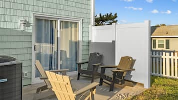 A covered patio with Adirondack chairs, a heater, and a sliding glass door.