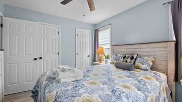 A bedroom with a bed, a ceiling fan, a window with curtains, and a nightstand with a lamp.