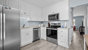 A modern kitchen with white cabinets, stainless steel appliances, and a wooden floor. - Oceanside Condo in Atlantic Beach, NC-Anchors Away Unit 3 (Atlantic Beach)