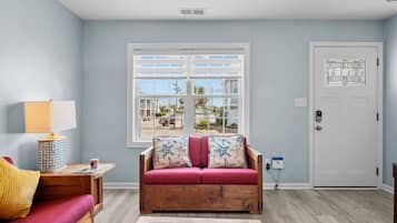 A living room with a wooden sofa, a red armchair, a lamp, and a window with a view of houses.