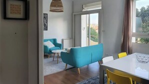 A modern living room with a blue sofa, a white dining table, and yellow chairs. - Quiet villa top with shared pool. Close to port and beaches. (Toulon)