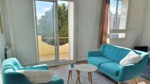 A modern living room with teal sofas, a wicker ottoman, and a glass door leading to a balcony. - Quiet villa top with shared pool. Close to port and beaches. (Toulon)