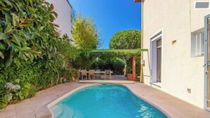 A swimming pool with a curved edge, surrounded by a patio area with chairs and a table. - Quiet villa top with shared pool. Close to port and beaches. (Toulon)