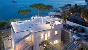Une maison moderne à deux étages, dotée d’une terrasse sur le toit, d’une piscine et offrant une vue sur la mer.
