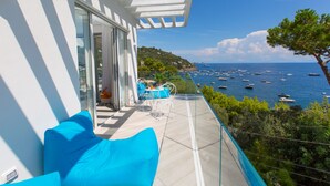 Un balcon doté d’une rambarde en verre, donnant sur une zone côtière où se trouvent des bateaux.
