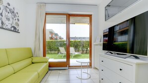 Sala moderna com sofá verde, TV em um móvel branco e porta de vidro deslizante que dá para uma varanda com móveis de exterior.