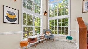 A room with large windows, a chair, a small table, and a stool. - 8 Bedroom MANSION Biltmore Lake with Hot Tub. (Biltmore Lake)