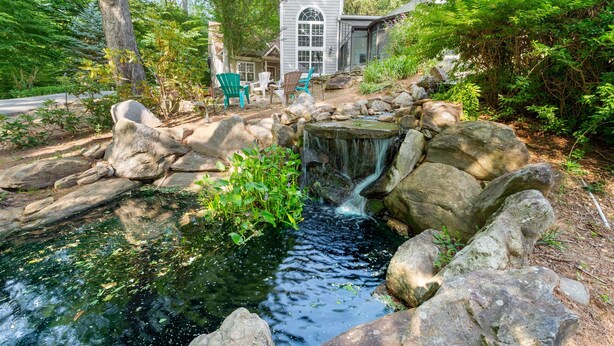 A pond with a waterfall, surrounded by rocks and greenery, with a house and chairs in the background. - 8 Bedroom MANSION Biltmore Lake with Hot Tub. (Biltmore Lake)