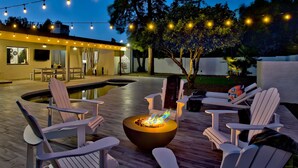 Una terraza al aire libre con sillas Adirondack, un hogar para fuego y luces colgantes.
