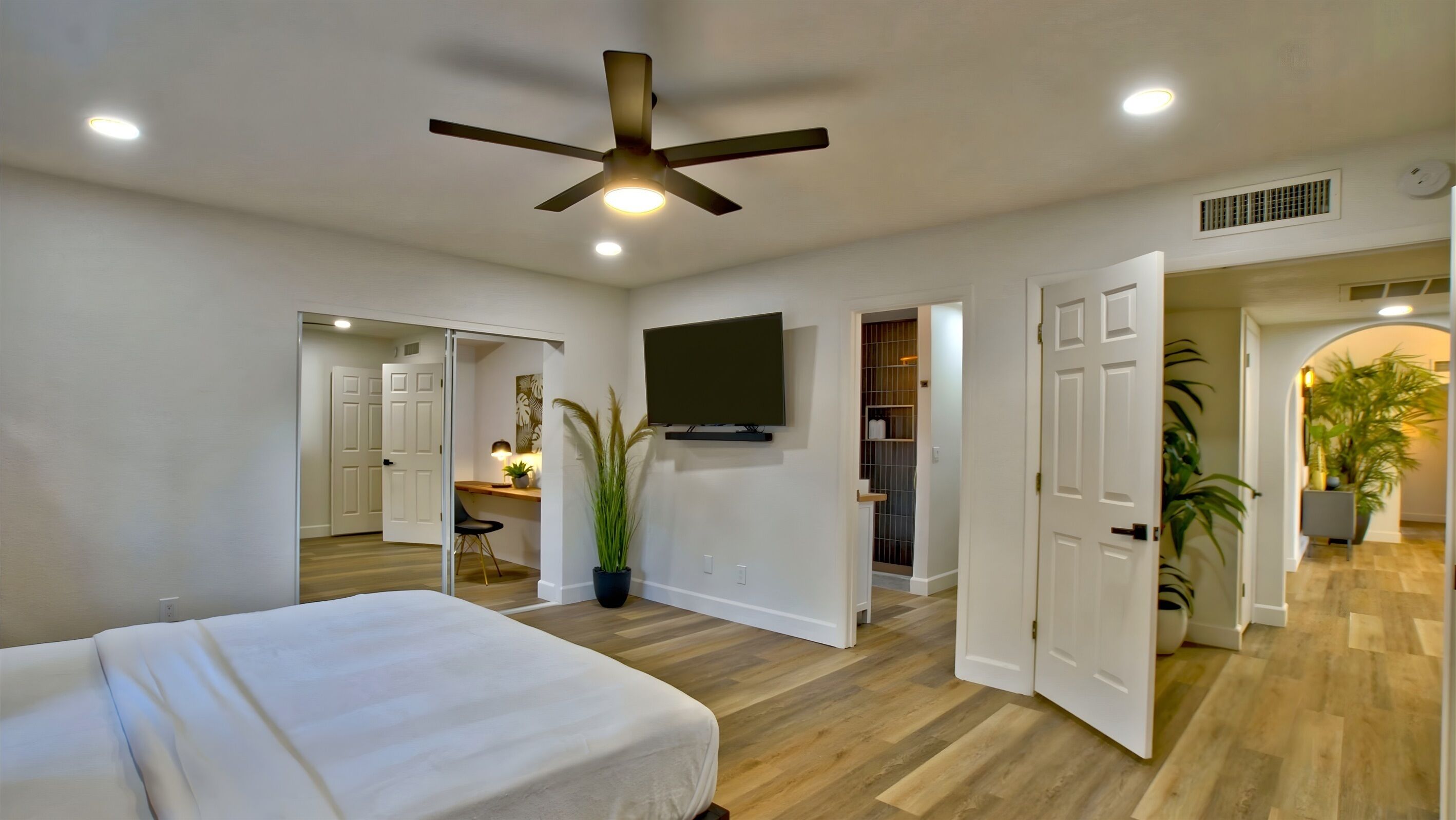 A bedroom with a bed, a ceiling fan, a TV, and a desk with a chair.