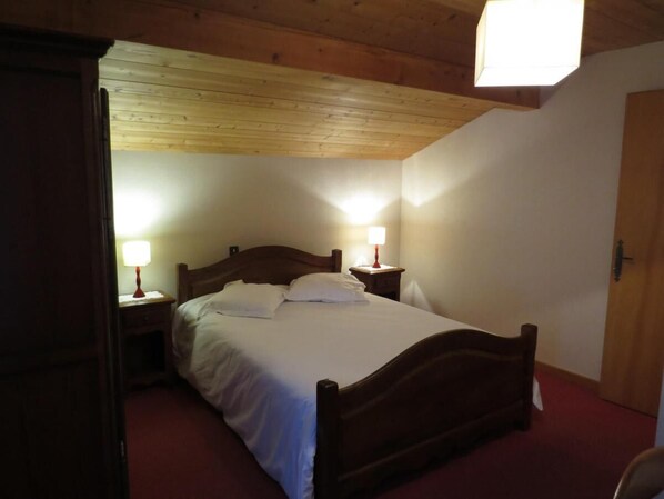 A single bed with a wooden headboard, two bedside tables with lamps, and a door to the right.