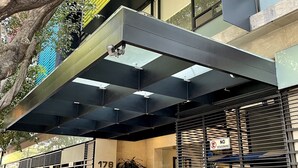 Un edificio moderno con acceso cubierto, un árbol grande y un cartel que indica prohibido estacionar.