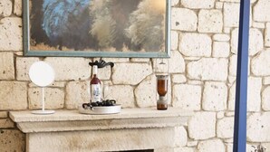 A stone fireplace with a framed abstract painting above it, a round mirror, and a small table with a magazine and sunglasses. - Puka Otel Alacatı (Cesme)