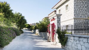 A stone building with a tiled roof, a sign reading "PURA HOTEL," and a paved pathway lined with greenery and flowers. - Puka Otel Alacatı (Cesme)
