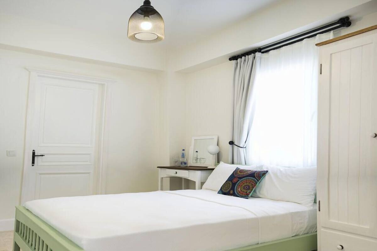 A bedroom with a bed, a nightstand, a wardrobe, a window with curtains, and a hanging light fixture.