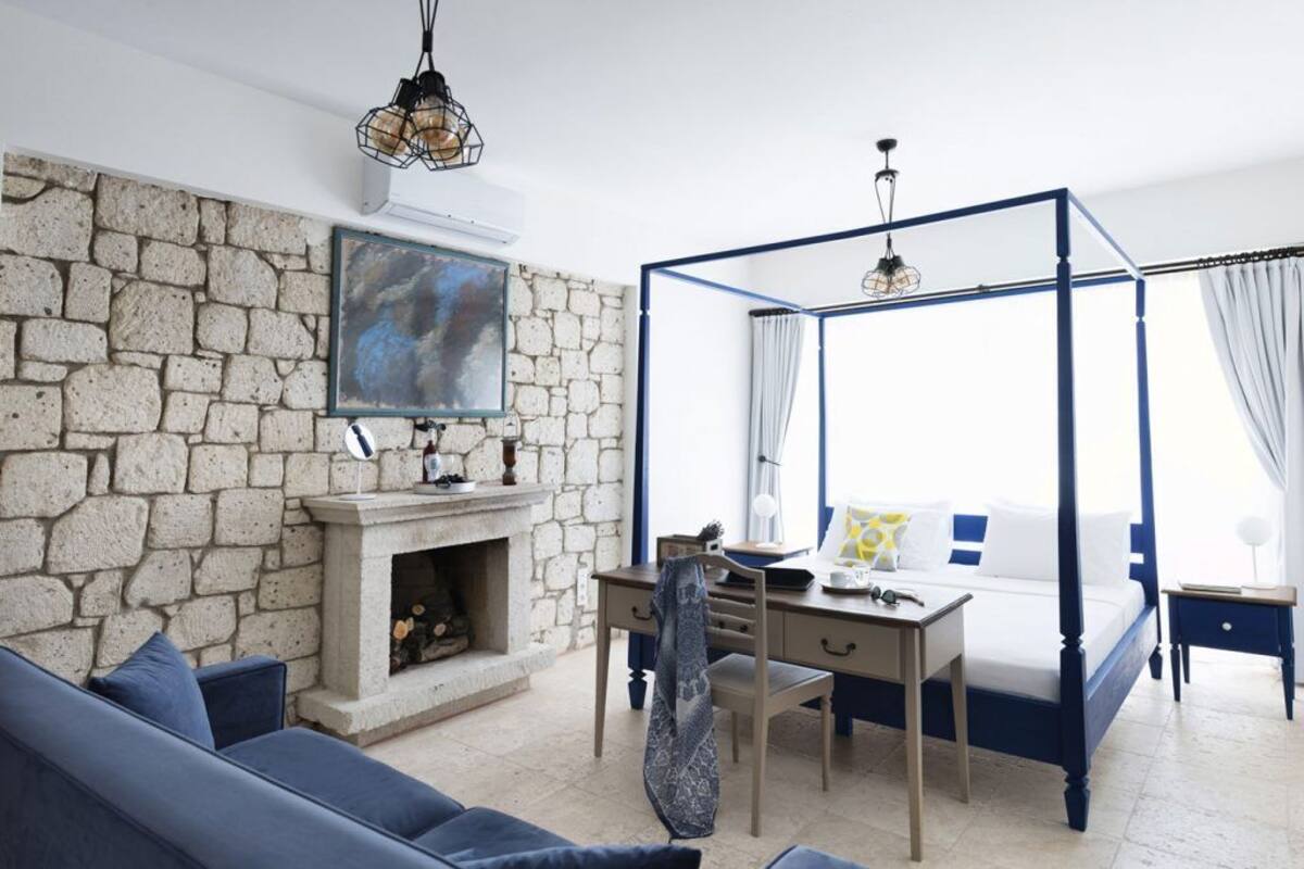 A bedroom with a stone wall, a four-poster bed, a desk, and a fireplace.