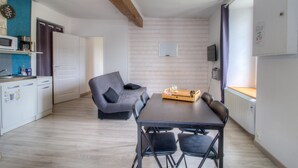Et kompakt køkken med moderne hårde hvidevarer, et spiseområde med bord og stole, og et hyggeligt opholdsområde med en sofa.
