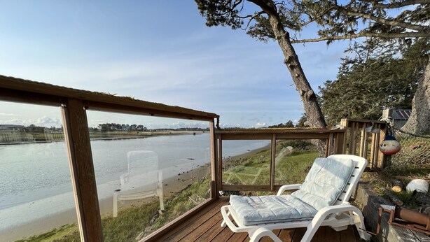 Een houten terras met een witte lounge stoel en uitzicht op een rivier.