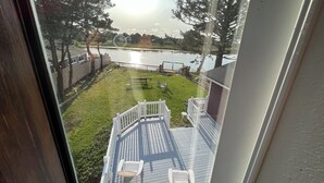 Uitzicht vanuit een raam op een achtertuin met een houten terras, een gazon en een waterpartij.