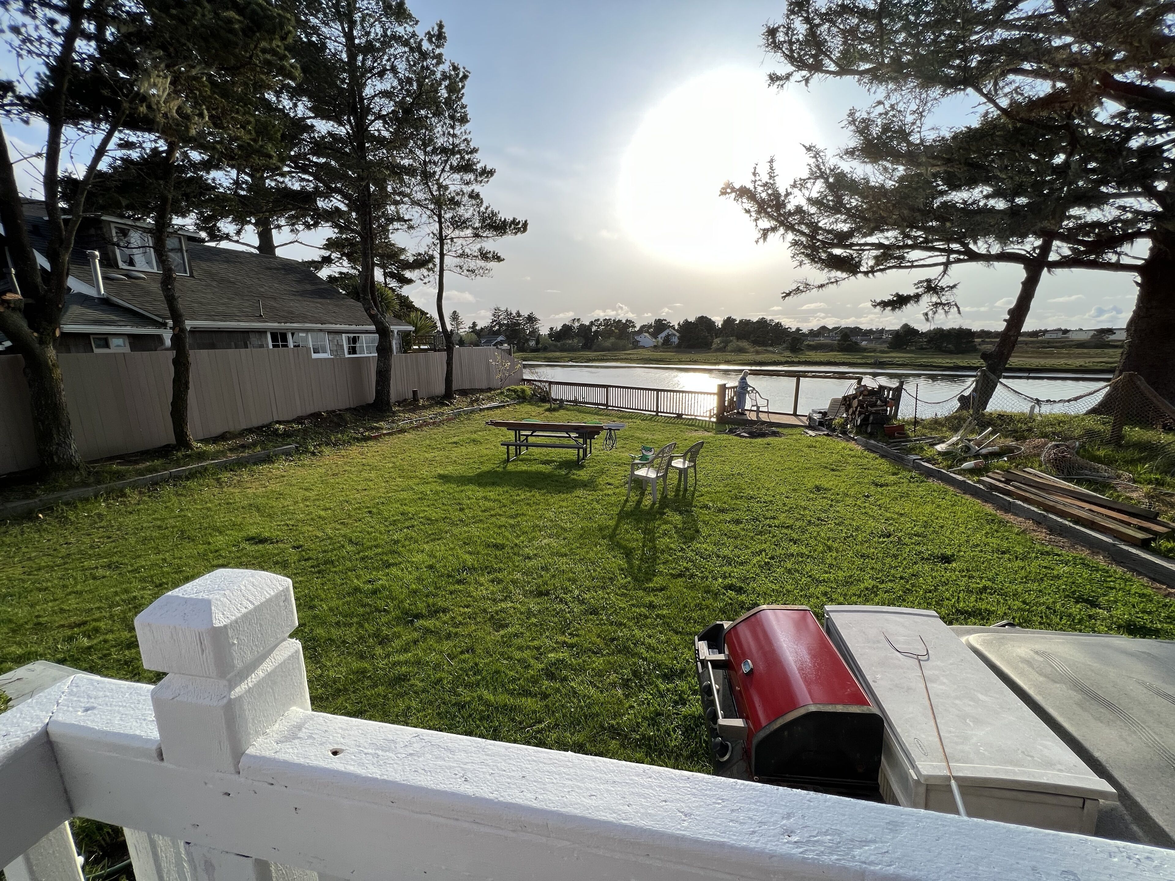 Un patio trasero con césped, una mesa de picnic, una barbacoa roja y vistas a un lago.