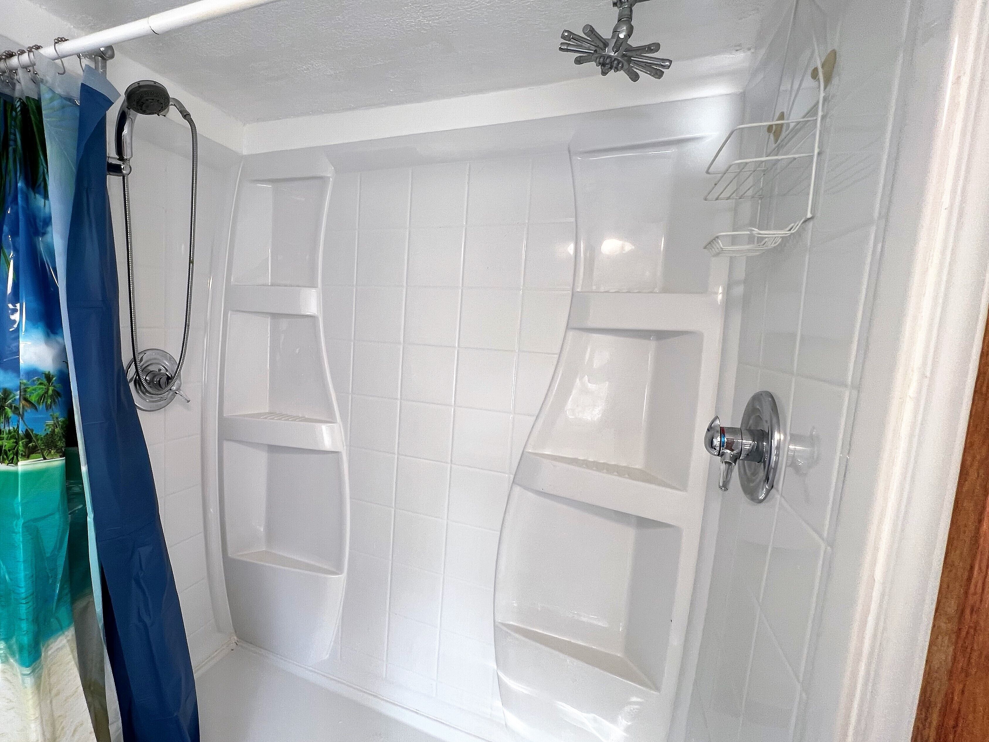 A bathroom with white tiled walls, a shower with a handheld showerhead, and a blue shower curtain.