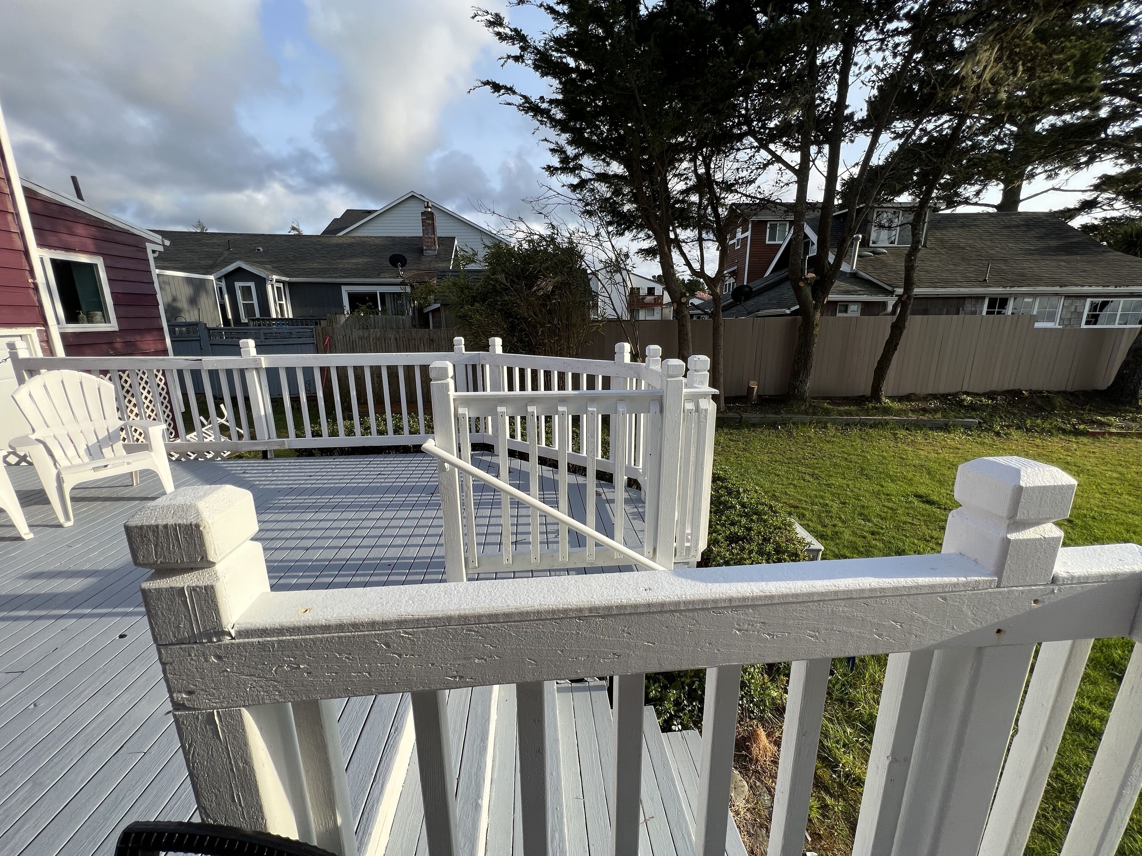 Una terraza de madera con barandal blanco, una silla Adirondack blanca y una jardinera de piedra.