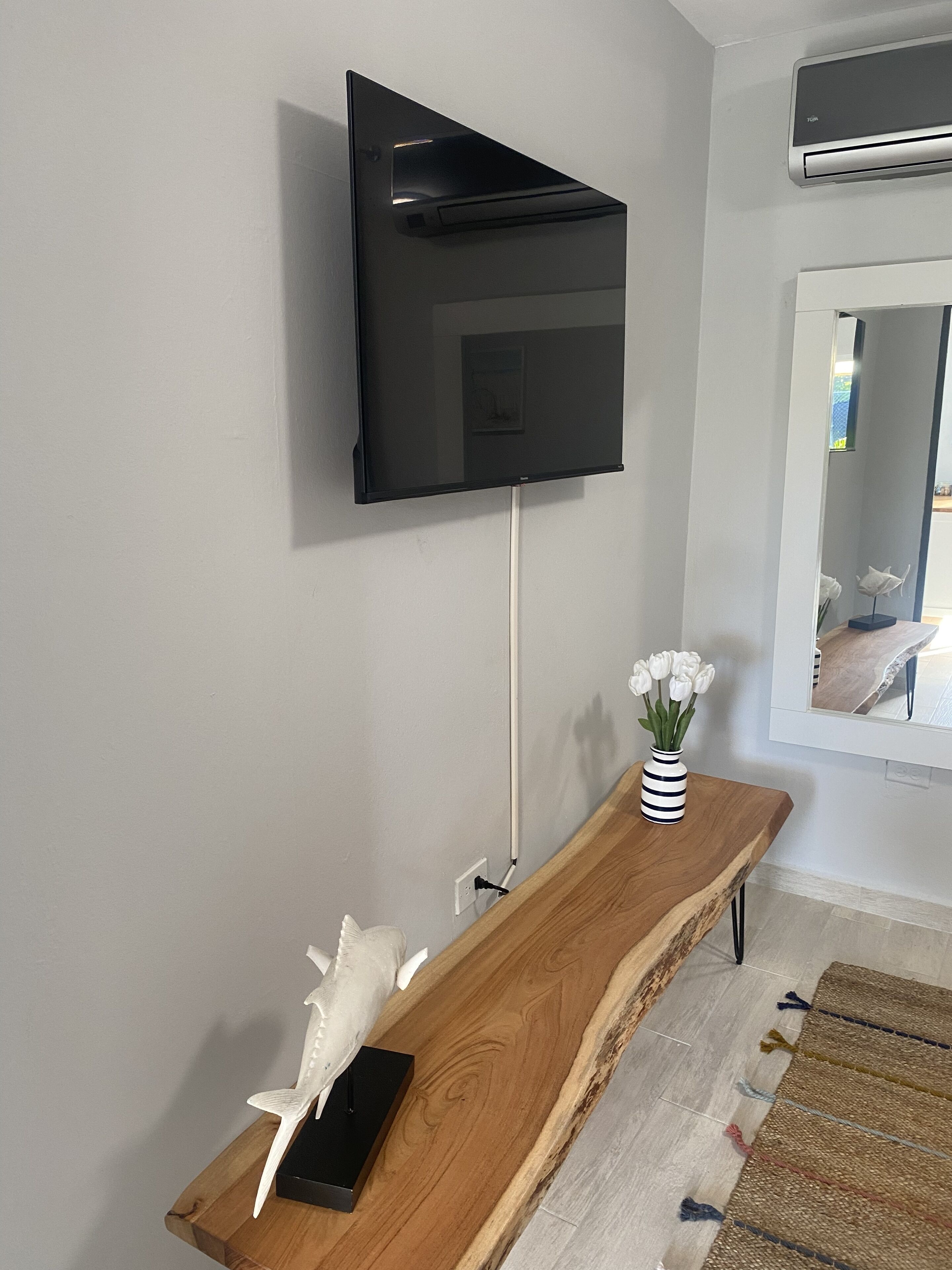 A modern living room with a mounted flat-screen TV, a wooden console table with decorative items, and a view through a doorway.