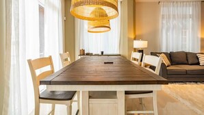 Un comedor con una mesa y sillas de madera, una lámpara colgante de mimbre y un sofá al fondo.