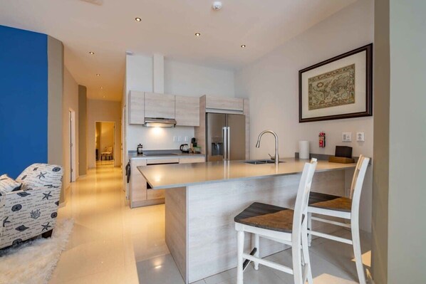 Una cocina moderna con una isla central, muebles blancos y electrodomésticos de acero inoxidable.