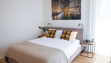 Een moderne hotelkamer met een groot bed, een nachtkastje, een klein tafeltje met een plant en een stadslandschap op de muur.