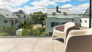A balcony with two chairs, a view of modern buildings, and a parked van. - Reckenthal House (Strassen)