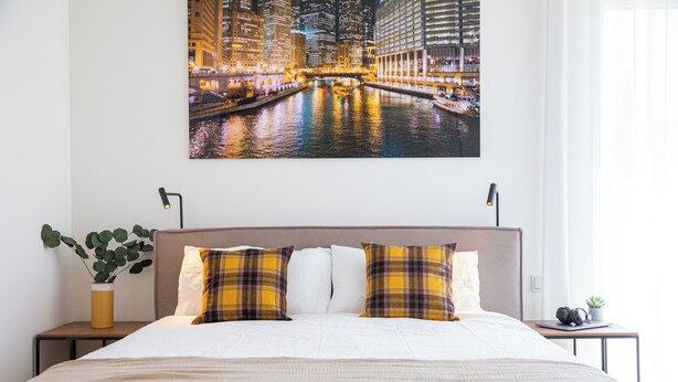 A hotel room with a large bed, a nightstand with a plant, and a cityscape view on the wall. - Reckenthal House (Strassen)