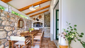 Un comedor con paredes de piedra, una mesa y sillas de madera, una chimenea de piedra y un jarrón con flores sobre una repisa de madera.