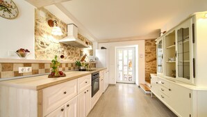 Una cocina con salpicadero de pared de piedra, armarios blancos y un mueble grande blanco con puertas de vidrio.