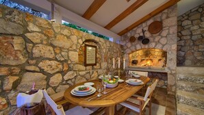 Una pared de piedra con chimenea, una mesa de madera dispuesta para comer y un ambiente rústico.