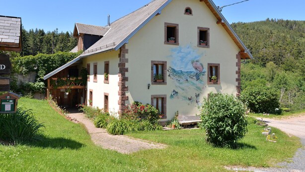 Ein traditionelles Chalet mit geneigtem Dach, Wandgemälde an der Seite und Eingangsbereich zum Garten.