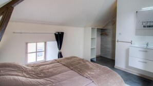 Ein Schlafzimmer mit Bett, einem Fenster mit Vorhängen, einem Kleiderschrank und einem Badezimmer mit Spiegel und Waschbecken.