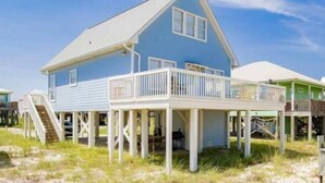 Una casa frente a la playa con balcón, una escalera que lleva a la terraza y una vista despejada del océano.