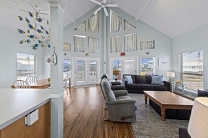 A spacious living room with a high ceiling, a ceiling fan, and a view of the outdoors through large windows. - Ocean Views, Remote beach, fisherman’s paradise (Gulf Shores)
