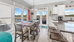 A spacious kitchen with a large island, wooden dining table, and chairs. There are large windows offering views of the outdoors. - Ocean+Lake Views~HEATED Pool~Pickleball~Golf Cart (Gulf Shores)