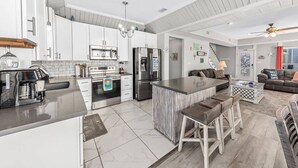 A modern kitchen with white cabinets, stainless steel appliances, and a central island with bar stools. - Ocean+Lake Views~HEATED Pool~Pickleball~Golf Cart (Gulf Shores)