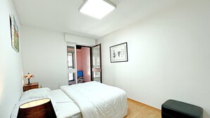 Un dormitorio con cama, mesita de noche, lámpara y un pequeño banco.