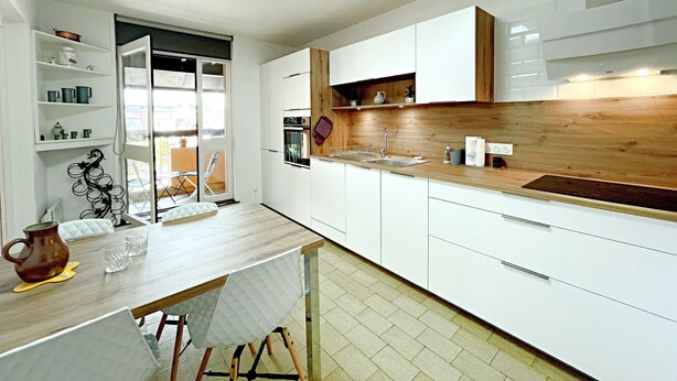 Una cocina moderna con armarios blancos, encimera de madera y un comedor con mesa y sillas.