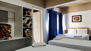 Habitación de hotel con dos camas, un armario, un ventilador de techo y una ventana con cortinas.