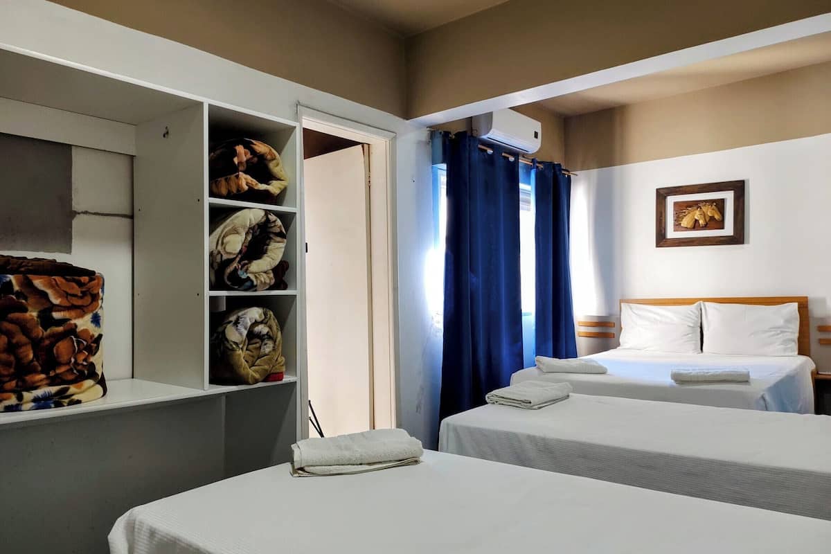 Een hotelkamer met twee bedden, een kledingkast, een plafondventilator en een raam met gordijnen.