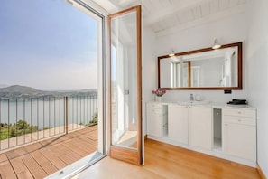 A modern bathroom with a large mirror, white cabinetry, and a view of a lake.