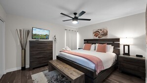 Ein Schlafzimmer mit Bett, Nachttischen, Deckenventilator, Fernseher und einer Holzbank.