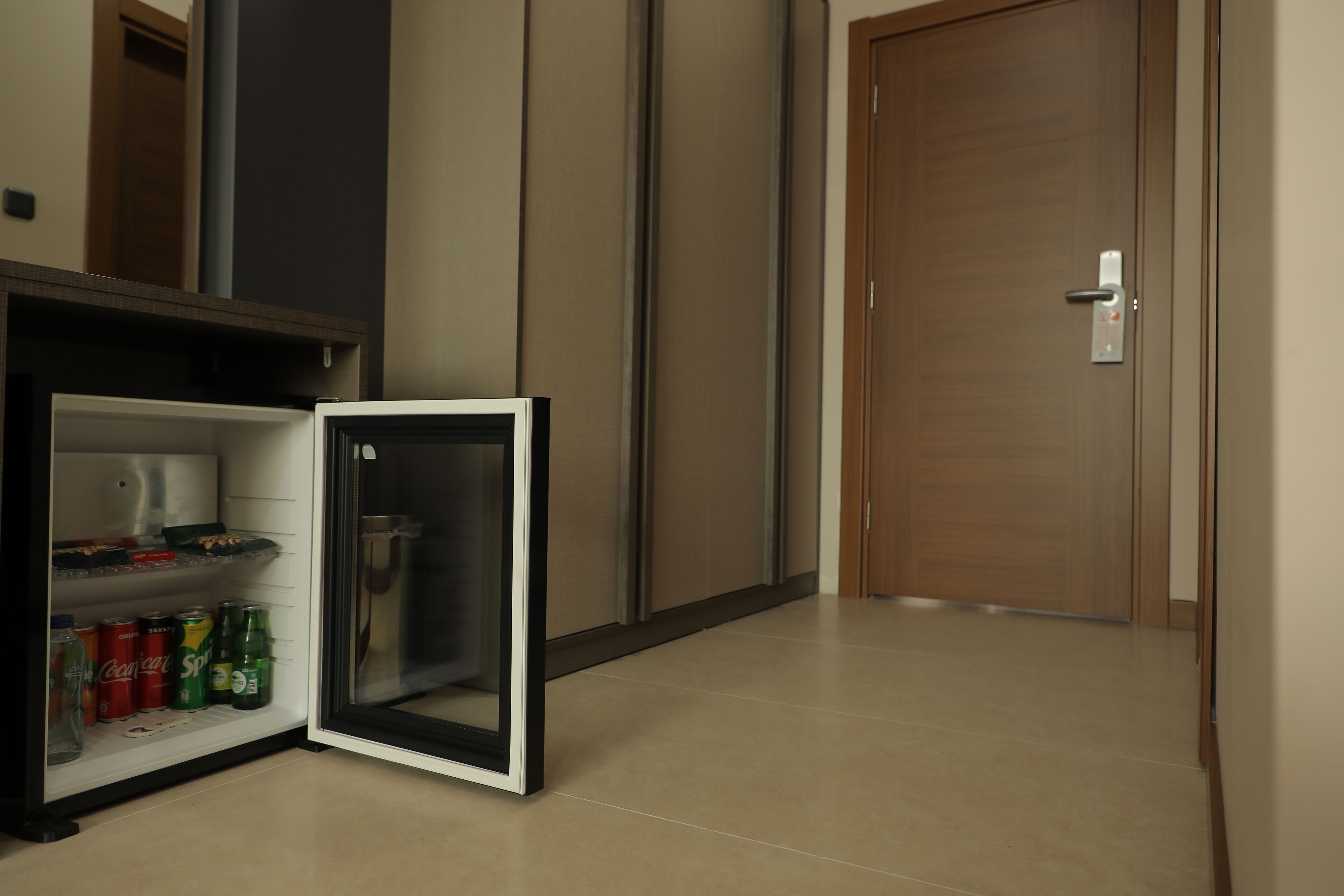 A compact refrigerator with beverages inside, located in a hallway with a wooden door and a tiled floor.